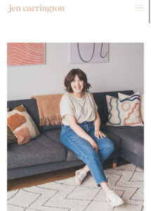 Jen Carrington, Business Coach sits on a sofa smiling at the camera